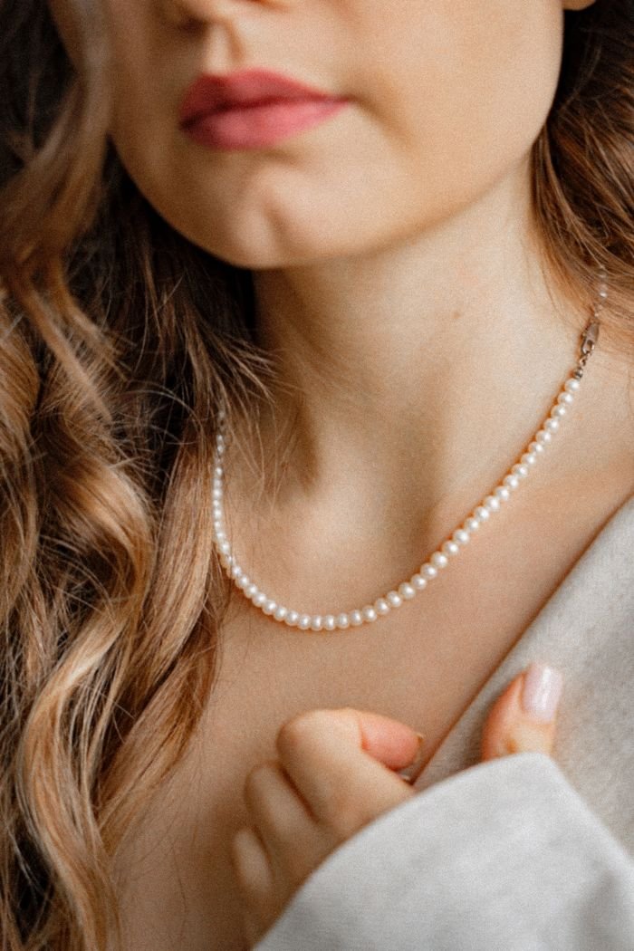 A close-up of a woman with luscious hair wearing a classic pearl necklace.